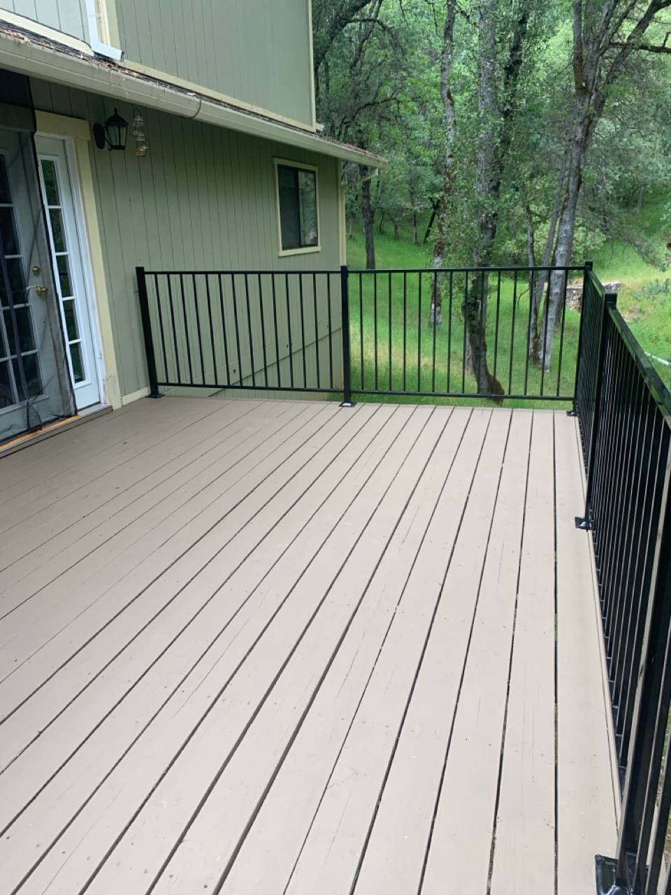 After: New light wooden deck with black metal railing overlooking a wooded yard
